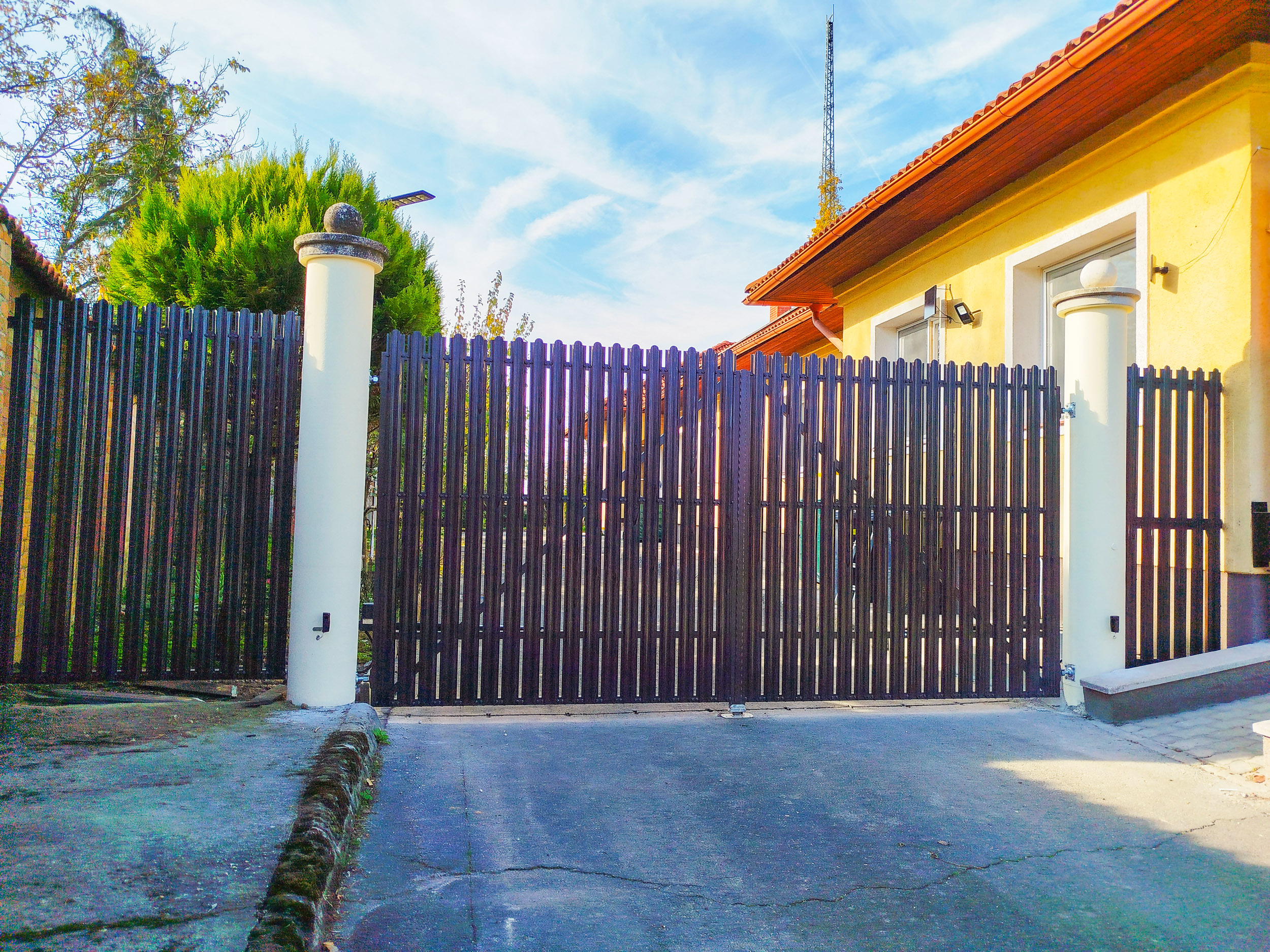 Fém kerítésléc tolókapu fehér oszloppal – bejárat